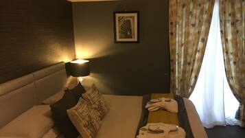 Habitación de hotel con cama, almohadas, un cuadro enmarcado en la pared, lámpara y ventana con cortinas.