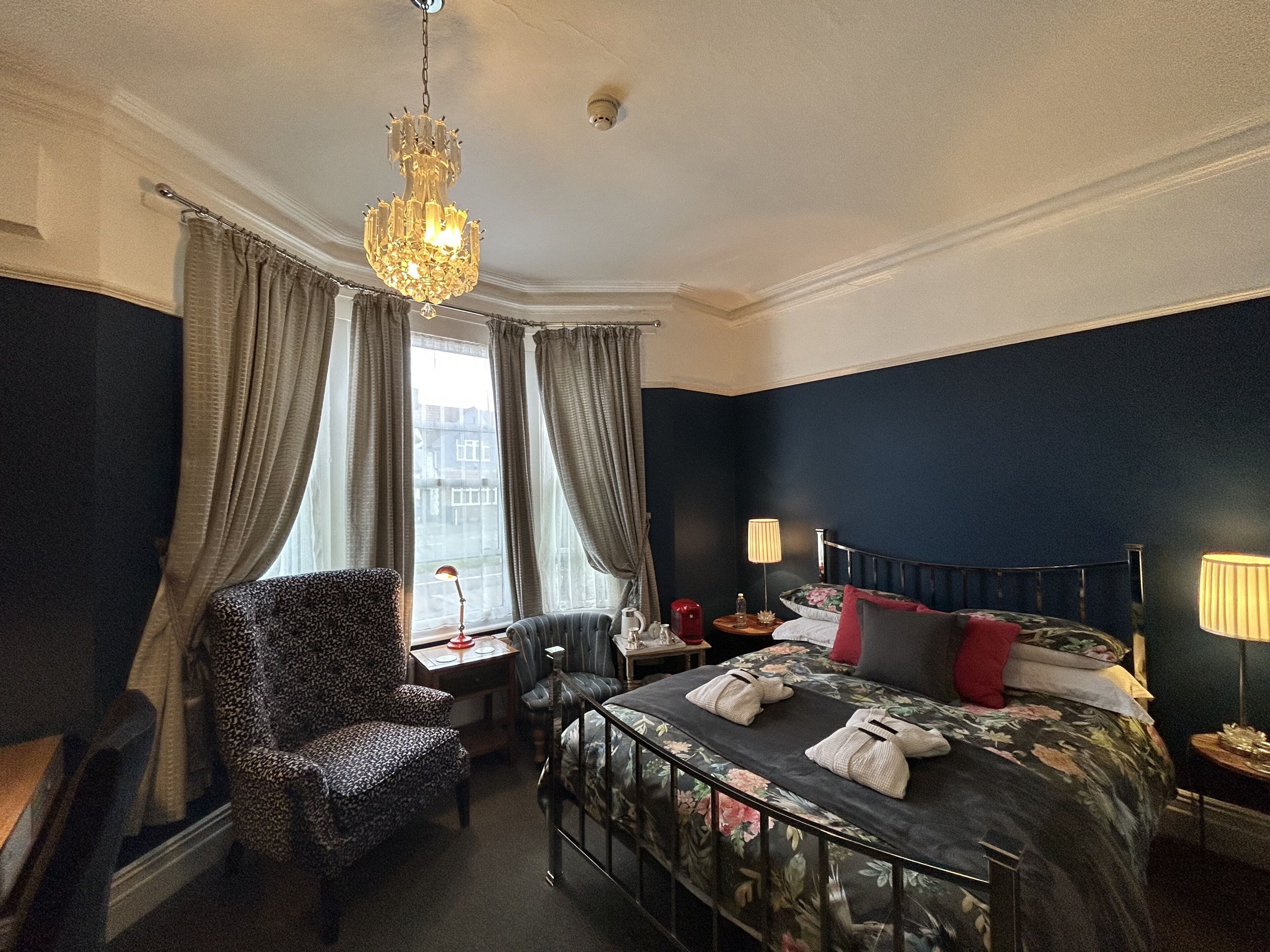 A hotel room with a bed, a chair, a desk, a lamp, and a window with curtains.
