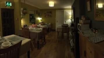 A restaurant with wooden tables and chairs, a kitchen area, and a bar with stools.