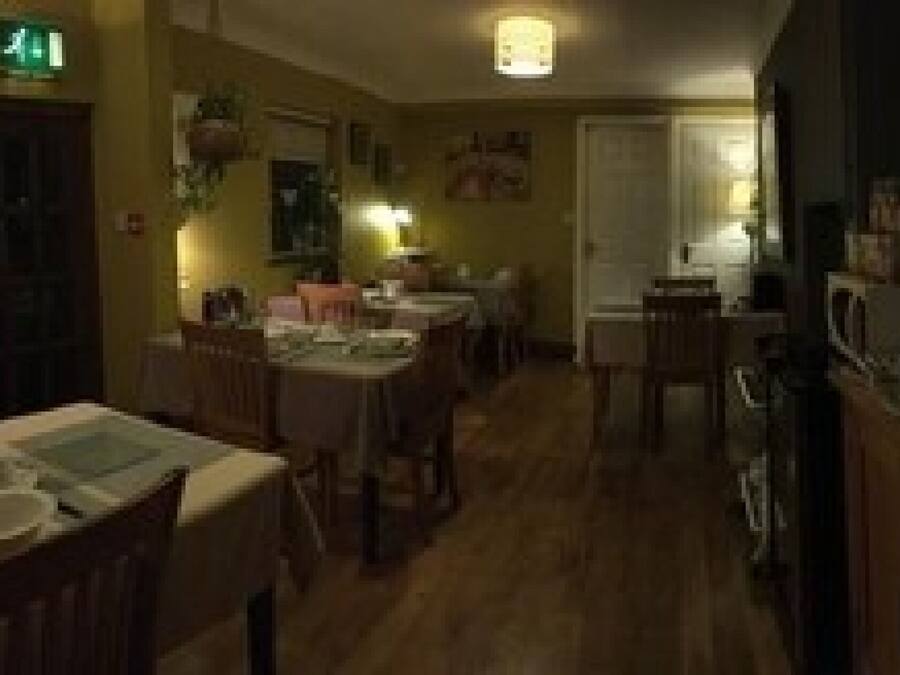 A restaurant with wooden tables and chairs, a kitchen area, and a bar with stools.