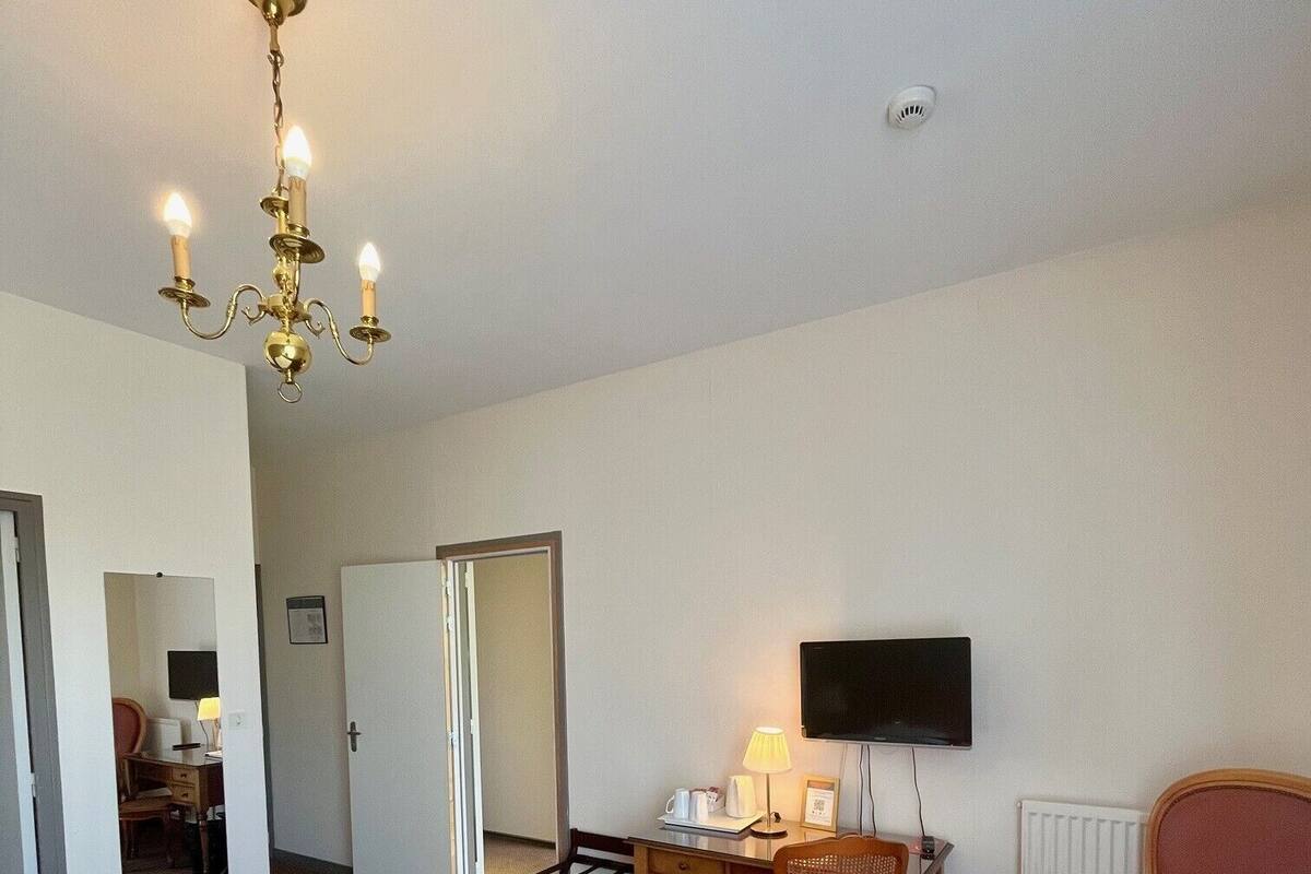 Una habitación de hotel con cama, escritorio, silla, televisión y un sillón rojo.