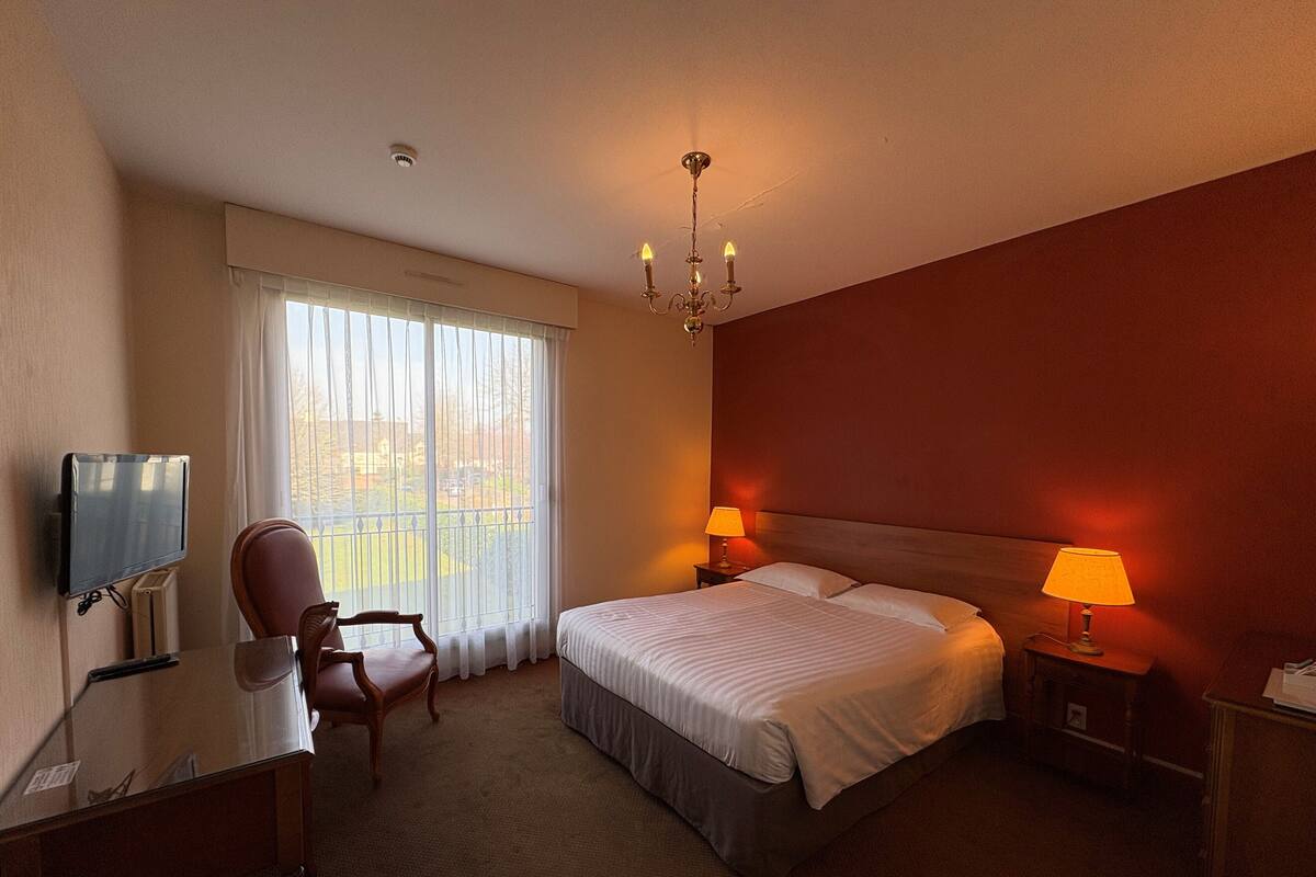 Habitación de hotel con una cama grande, dos lámparas de noche, un televisor, una silla y vistas al exterior a través de la ventana.