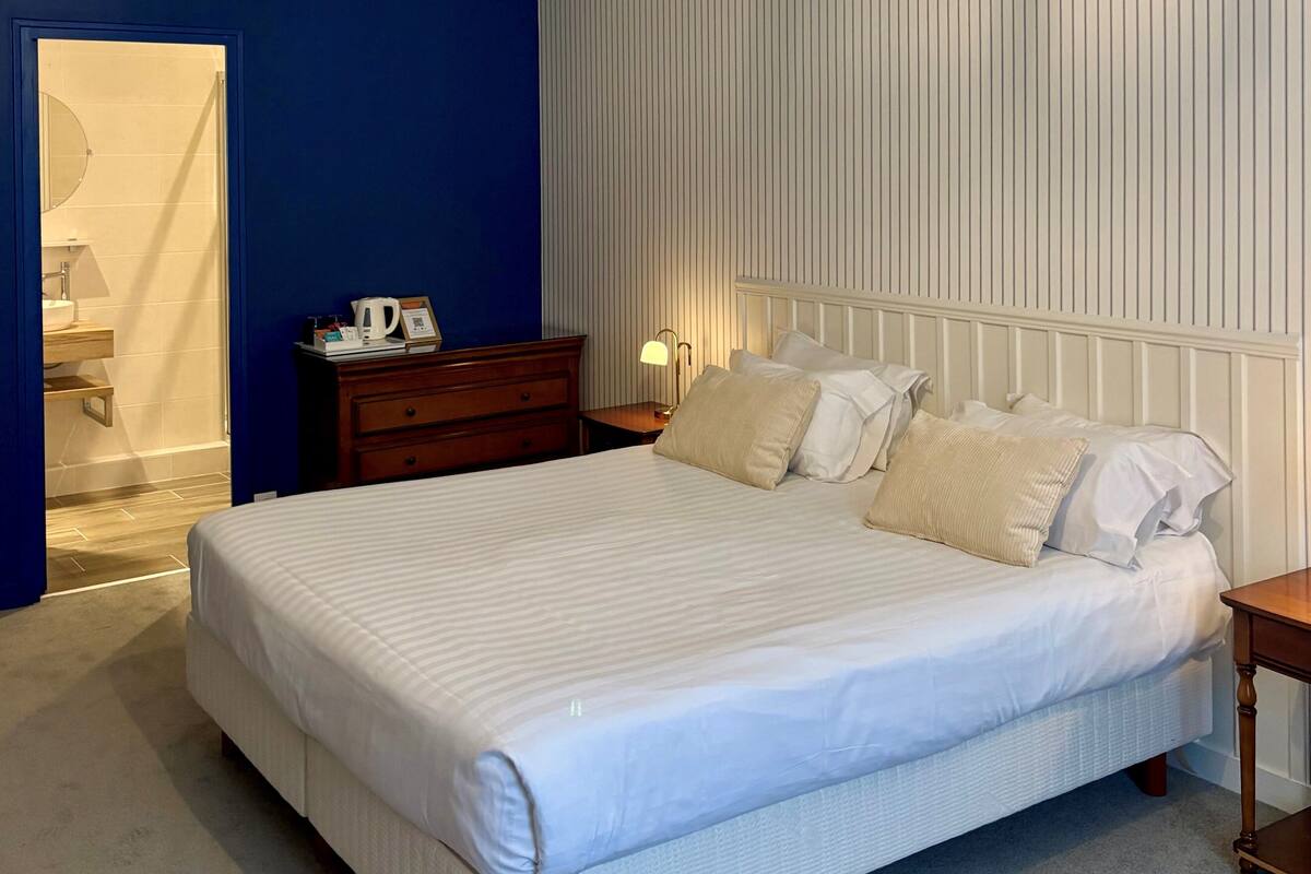 Un dormitorio con una cama grande, una mesita de noche de madera, una mesita con lámpara y una pared con paneles verticales.