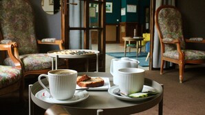 Un comedor con sillas de estampado floral, una mesa redonda con una bandeja que sostiene una taza, una tetera y una rebanada de tostada.