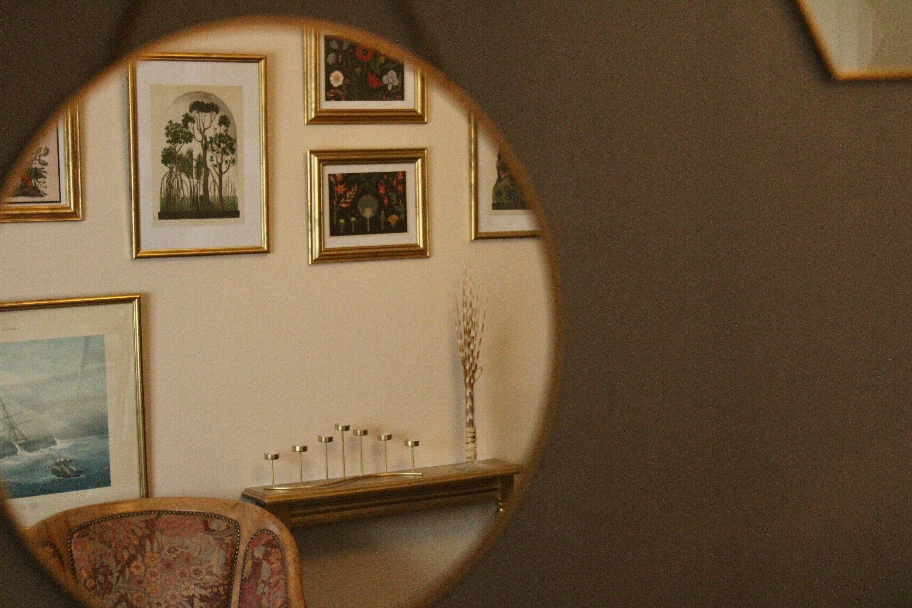 Ein Zimmer mit gerahmten Kunstwerken an der Wand, eine Holzkommode mit Kerzen und ein Stuhl mit Blumenmuster.