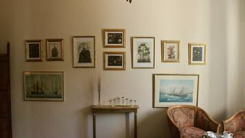 Ein Zimmer mit einer Bildergalerie an der Wand, einem kleinen Tisch mit einer Vase und Kerzen sowie zwei Polstersesseln mit Serviertablett.
