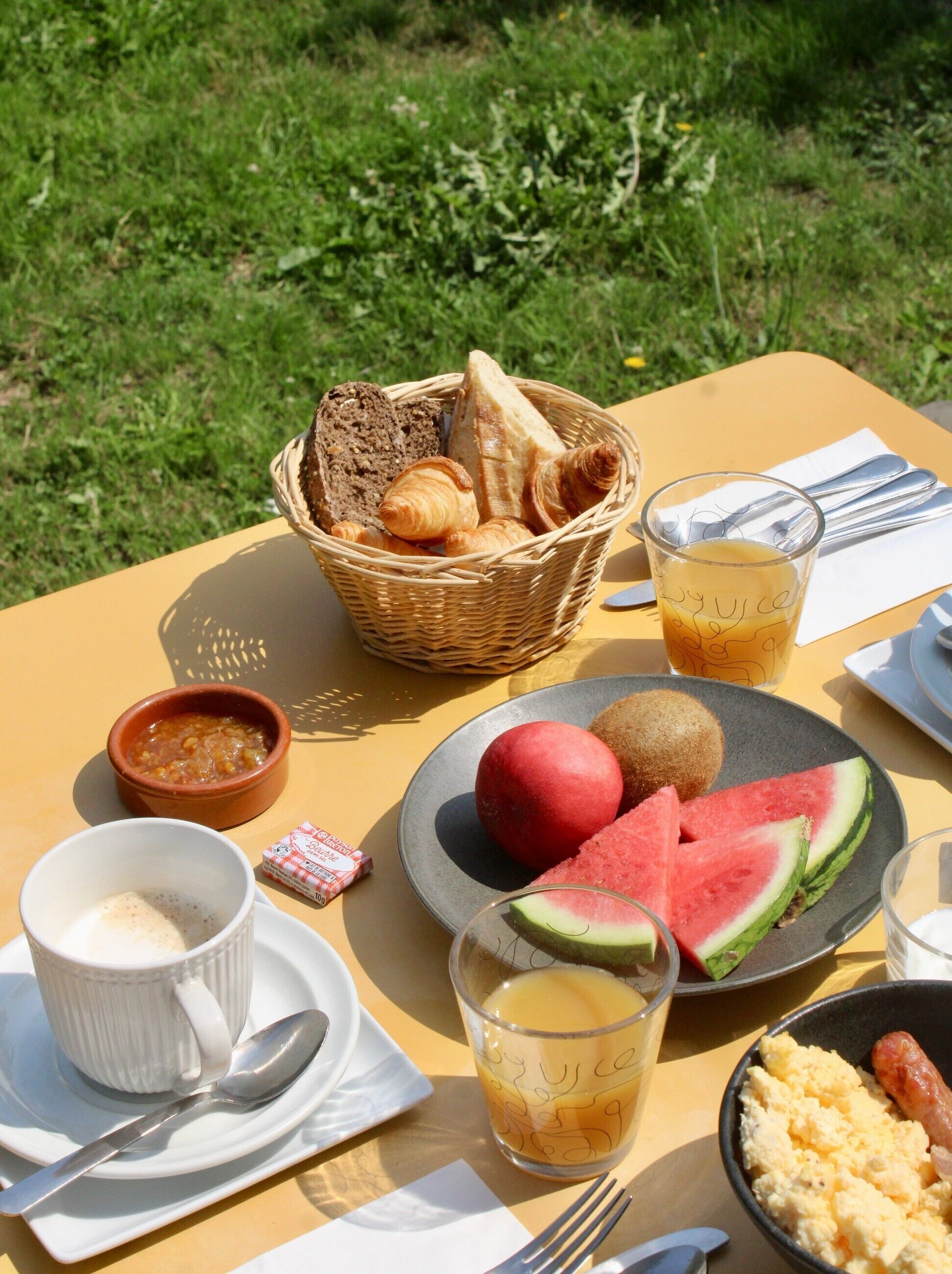 Ein Tisch mit Frühstücksleckereien, darunter Brot, Croissants, eine Schüssel Suppe, ein Teller mit Wassermelone, ein Glas Orangensaft und eine Tasse Kaffee.