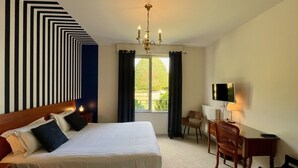 Habitación de hotel con cama, escritorio, silla, televisión y vistas al exterior.