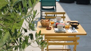 Un espacio al aire libre con zona de comedor, mesa lista para el desayuno, con pan, fruta y bebidas.
