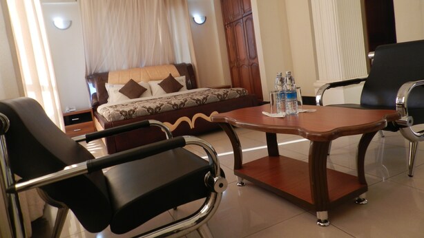 A hotel room with a bed, a sofa, a dining table, and two chairs. There are bottles on the table. - Hotel Jfrigh (Kampala)