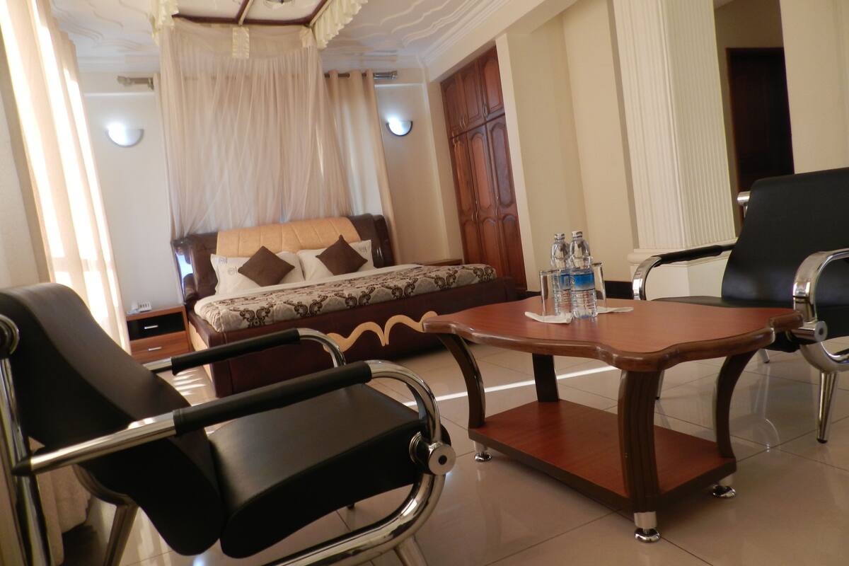 Habitación de hotel con cama, sofá, mesa de comedor y dos sillas. Hay botellas sobre la mesa.