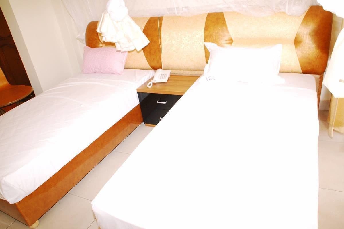 Una habitación de hotel con dos camas individuales, una mesita de noche con teléfono y un cajón pequeño.