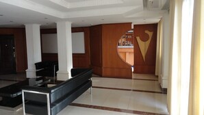 A spacious lobby with a black sofa, white columns, and a wooden reception desk. - Hotel Jfrigh (Kampala)