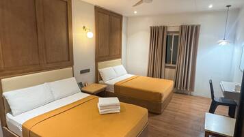 A hotel room with two beds, a ceiling fan, a desk, and a window with curtains.