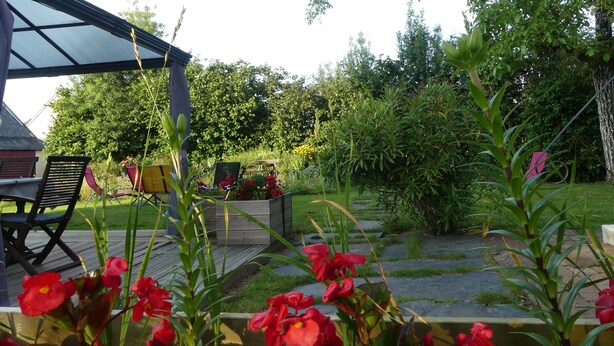 A garden with a wooden deck, outdoor seating, and various plants.