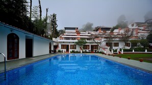Una piscina con borde de azulejos, rodeada por un edificio con varias ventanas y una escalera que sube a un nivel superior.