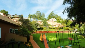 Un barrio residencial con un jardín césped, un columpio y un sendero que lleva a una casa con un muro de ladrillo rojo y ventanas.