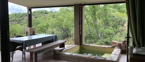 A patio area with a table and chairs, a stone hot tub, and a view of a forested hillside.