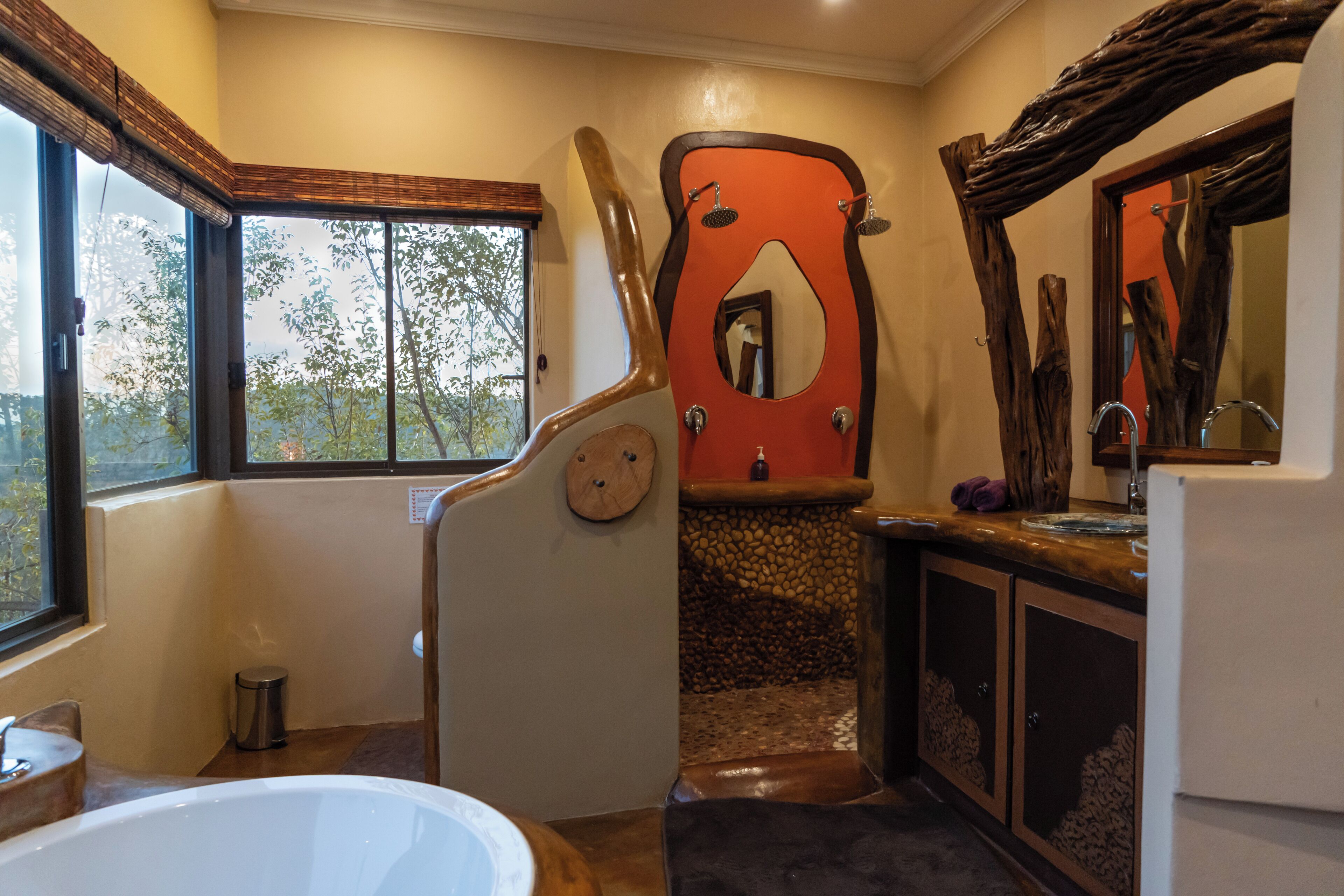 Une salle de bain avec une baignoire, un meuble-lavabo en bois, un miroir et une fenêtre donnant sur les arbres.