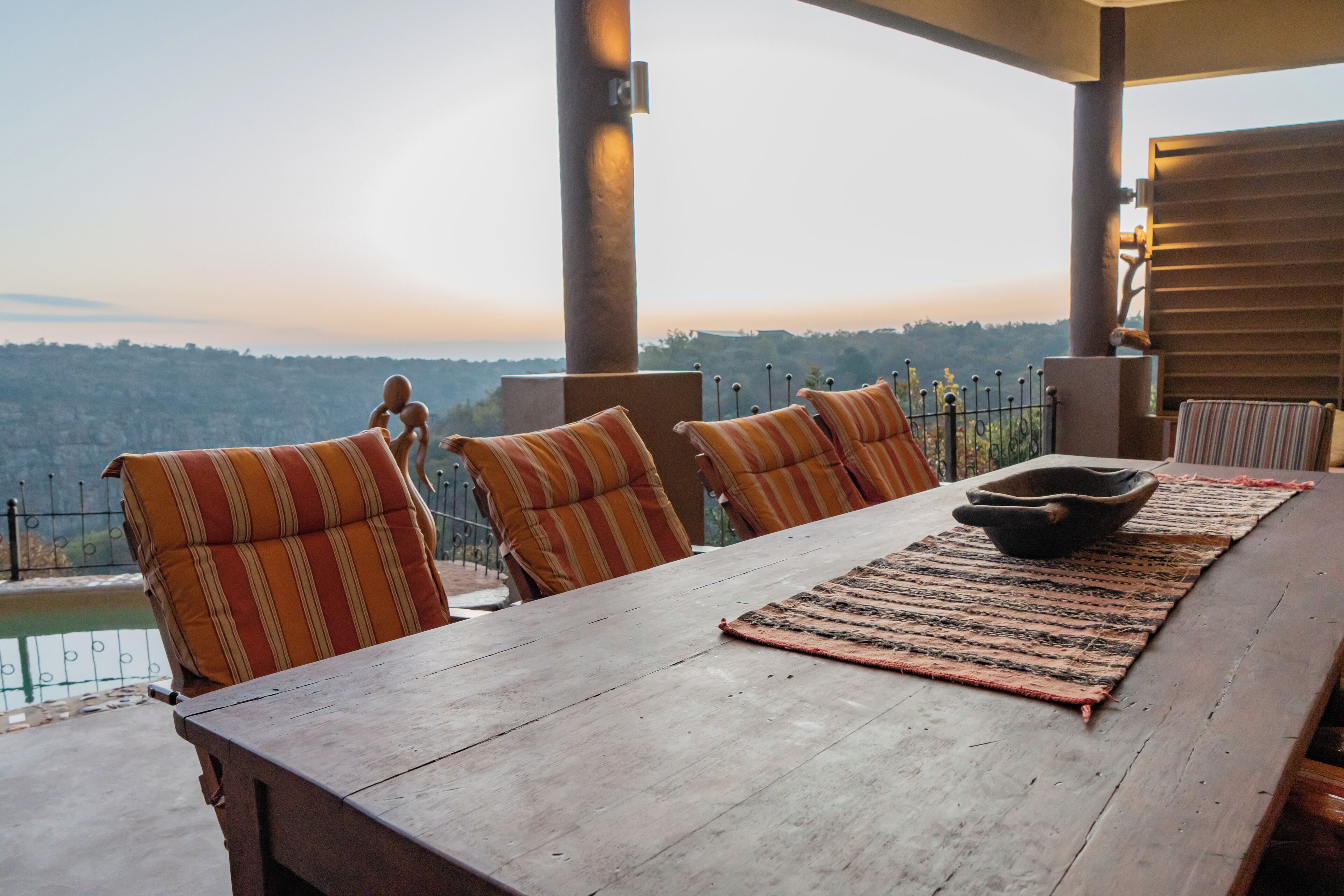 A wooden dining table with striped cushions, a woven placemat, and a bowl.