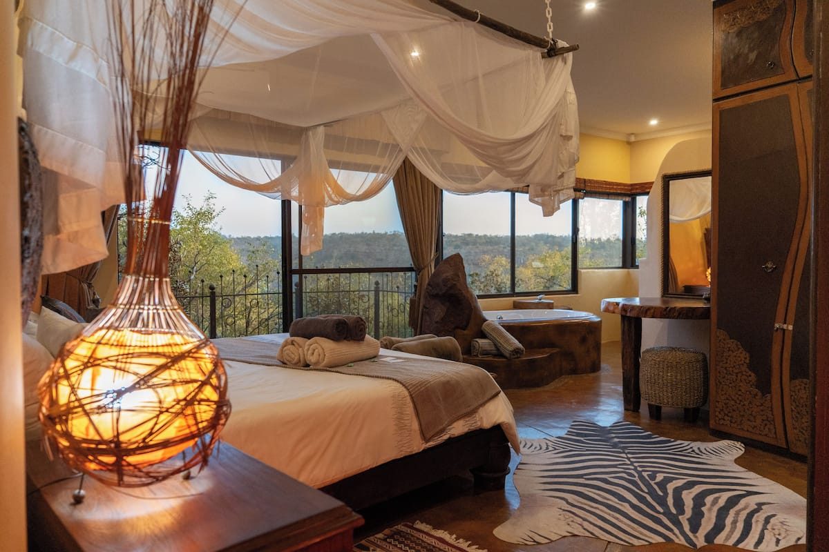 Ein Schlafzimmer mit einem großen Bett, einer Nachttischlampe, einem Zebra-Teppich und Blick ins Freie.