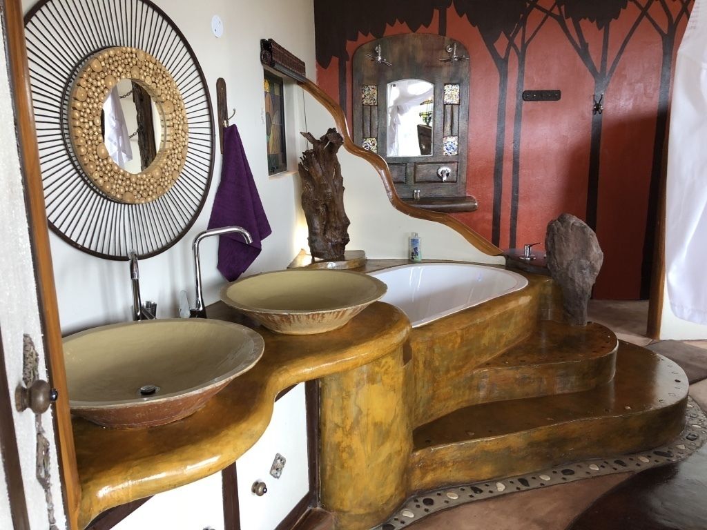 Un baño con un diseño singular, que incluye un espejo grande, dos lavamanos y una escultura de madera decorativa.