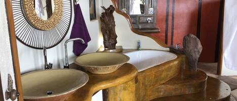 Un baño con un diseño singular, que incluye un espejo grande, dos lavamanos y una escultura de madera decorativa.