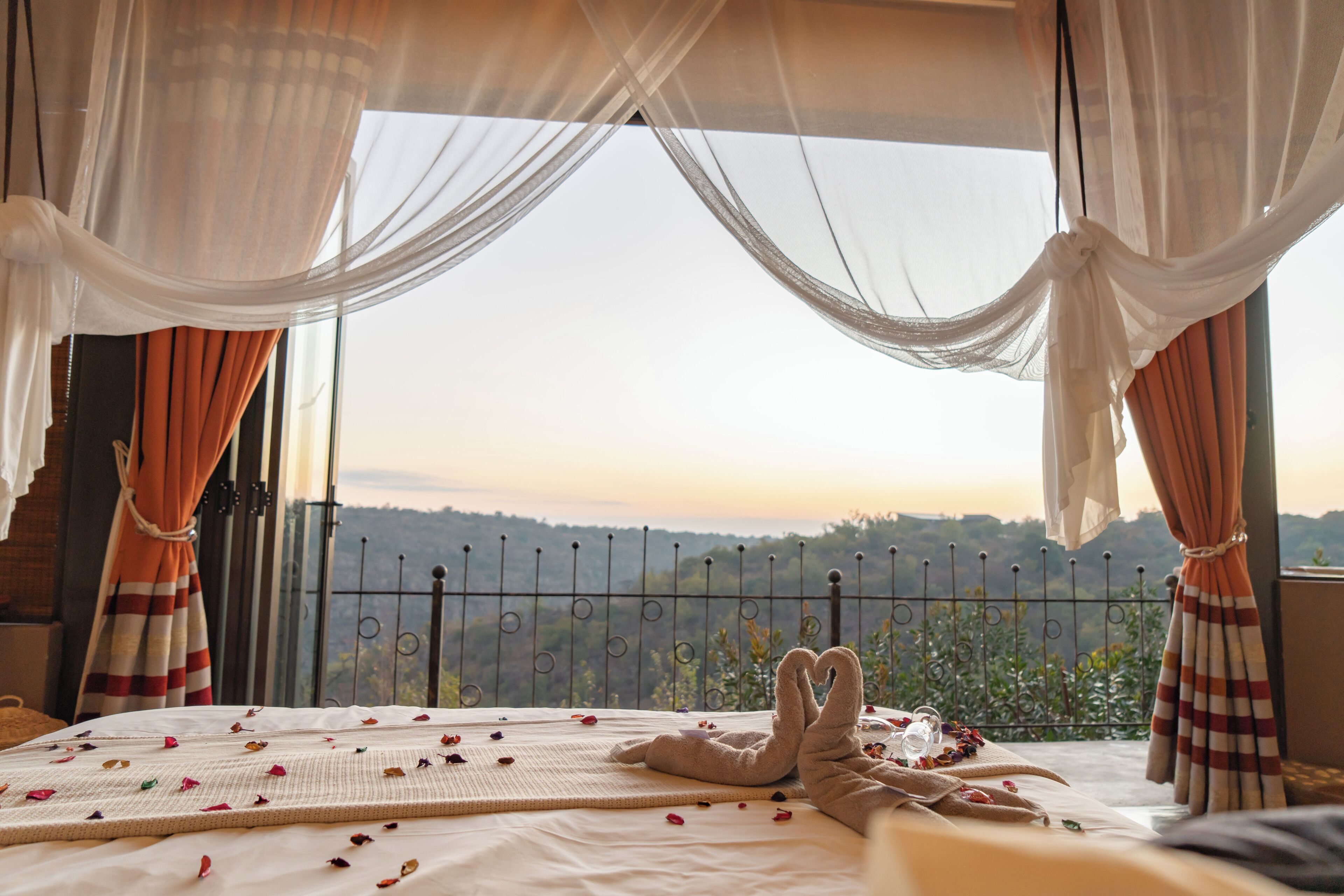 A bed with a view of a mountainous landscape, sheer curtains, and a metal fence.