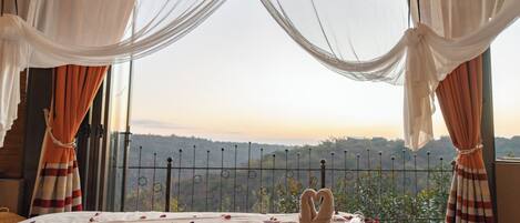 A bed with a view of a mountainous landscape, sheer curtains, and a metal fence.