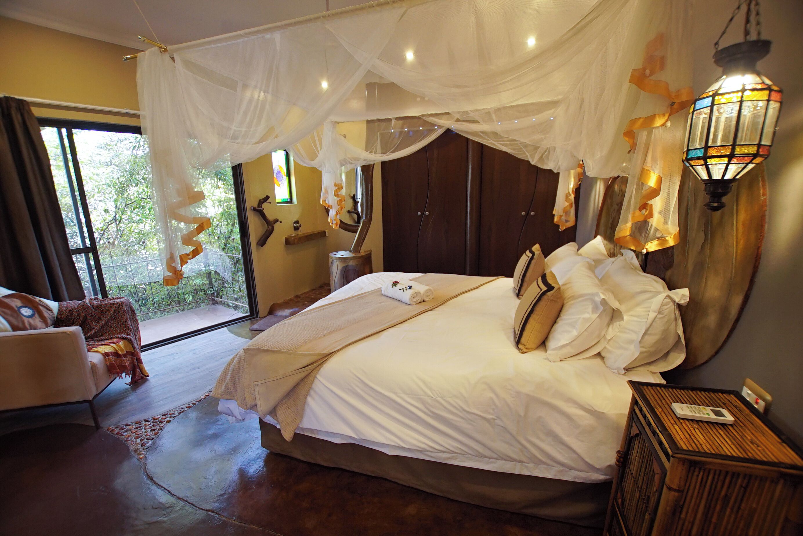 A bedroom with a large bed, a nightstand, a lamp, and a view of the outdoors.