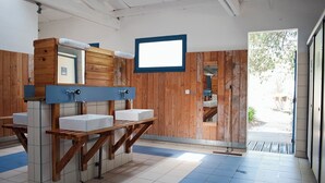 A public restroom with wooden partitions, multiple sinks, and a large mirror. - Huttopia Noirmoutier (Noirmoutier-en-l'Ile)