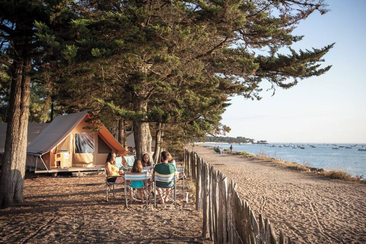 Un cadre idyllique au bord de la plage, avec une clôture en bois, une tente et un groupe de personnes assises sur des chaises.