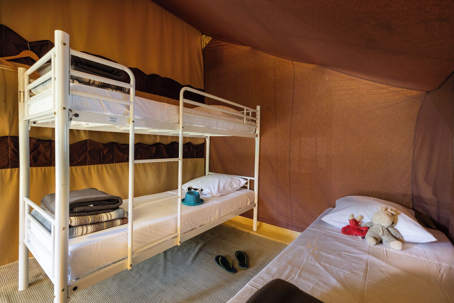 Habitación con literas, un colchón en la litera inferior, un par de zapatillas en el suelo y un oso de peluche en la cama de abajo.