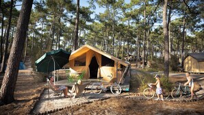 A forest campsite with a single wooden tent, a covered seating area, and bicycles. - Huttopia Noirmoutier (Noirmoutier-en-l'Ile)