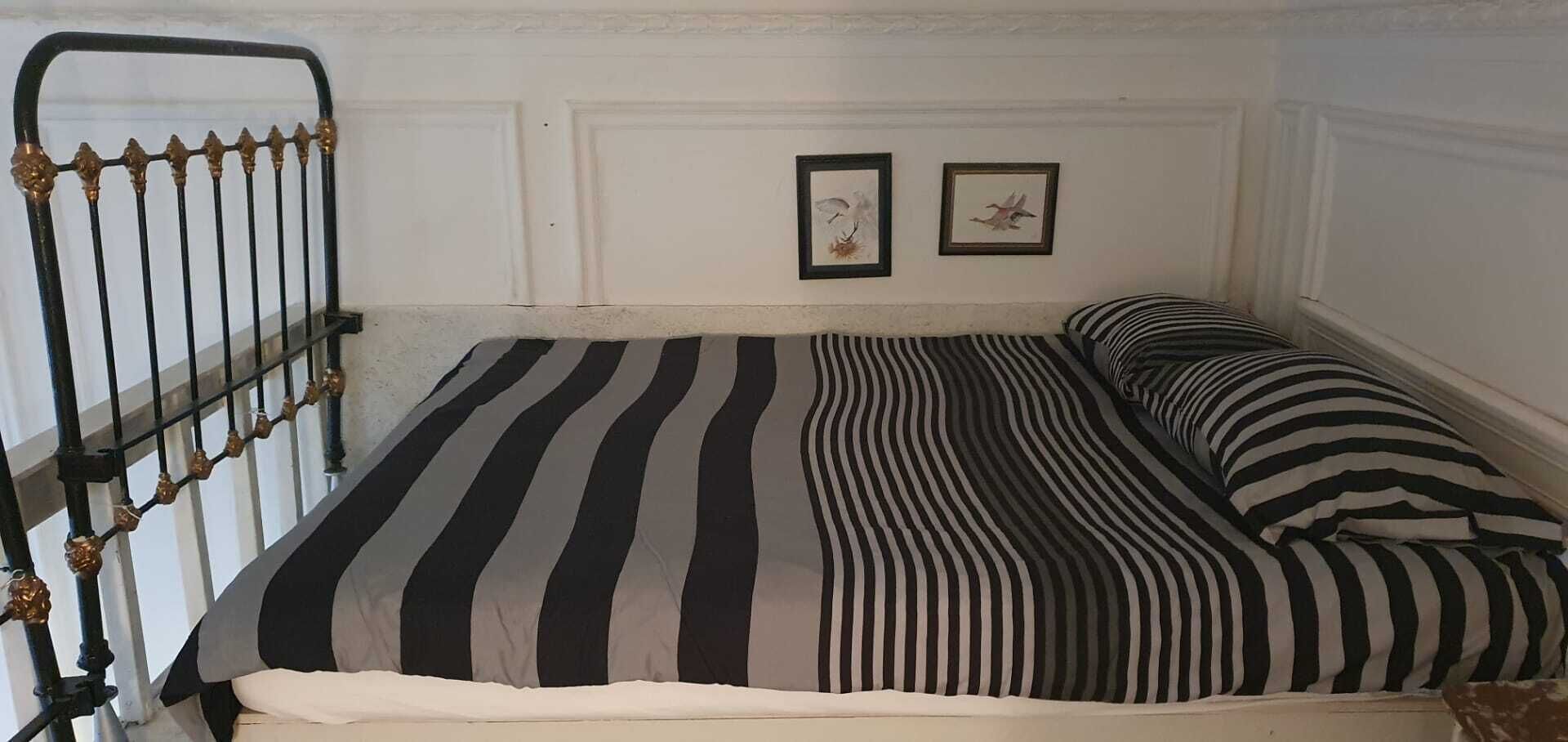 A single bed with a striped bedspread and matching pillows, a metal headboard, and two framed pictures on the wall.