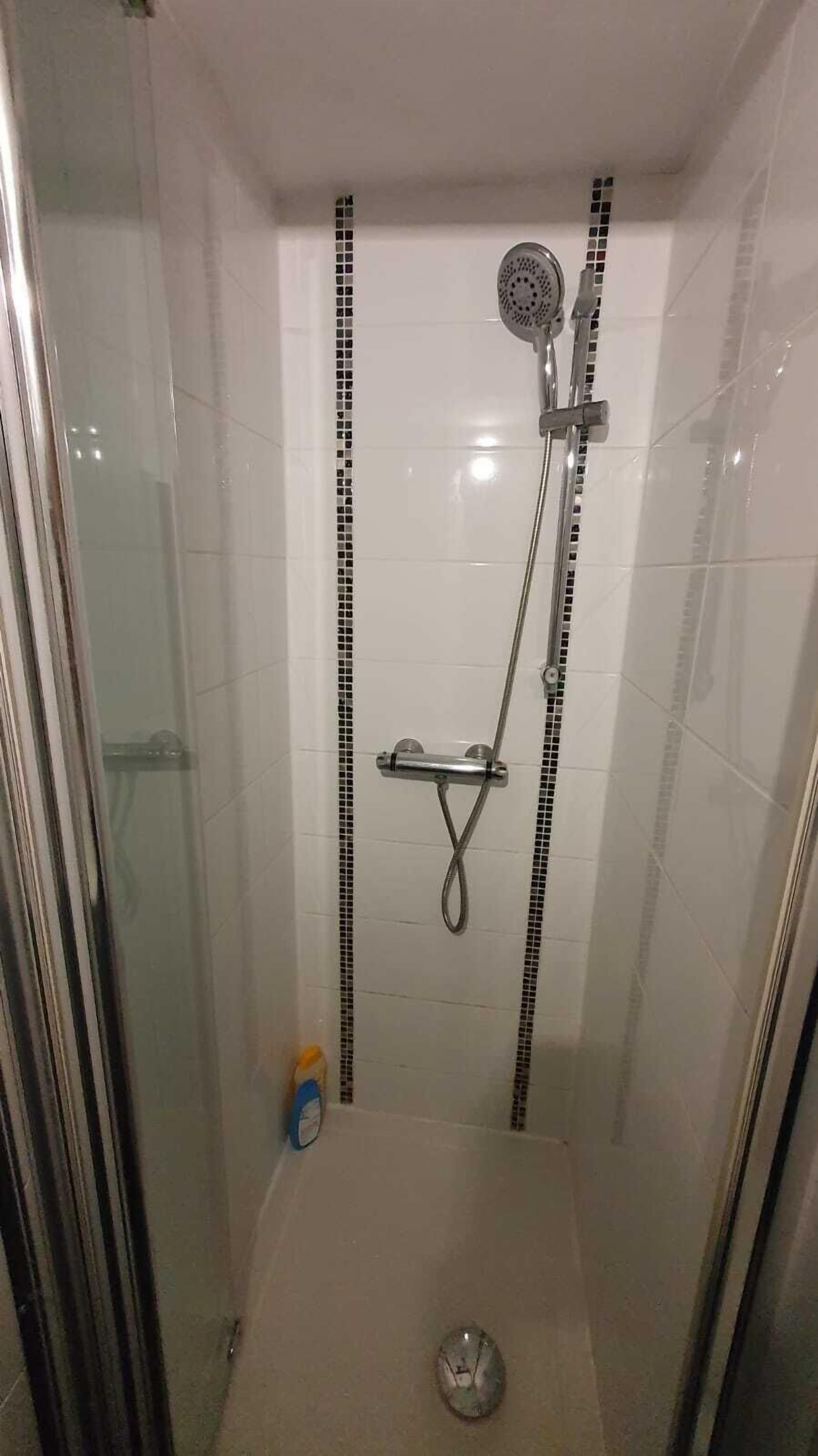 Un área de ducha pequeña y cerrada con puerta de vidrio, cabezal de ducha manual y grifo instalado en la pared.