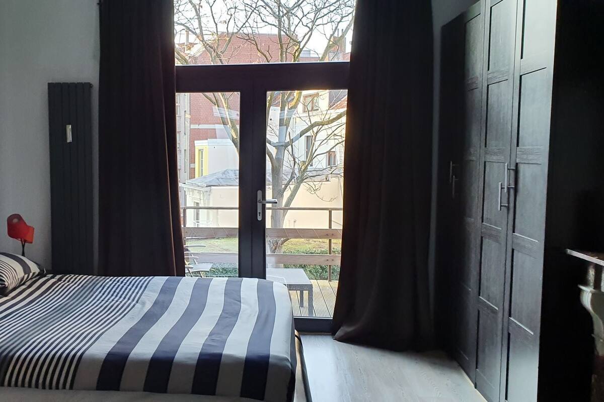 Un dormitorio con cama, una lámpara roja, un cartel enmarco y vistas al exterior.
