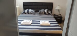 Ein ordentlich bezogenes Bett mit gestreifter Bettwäsche, zwei Kissen und zwei gefaltete Handtücher.