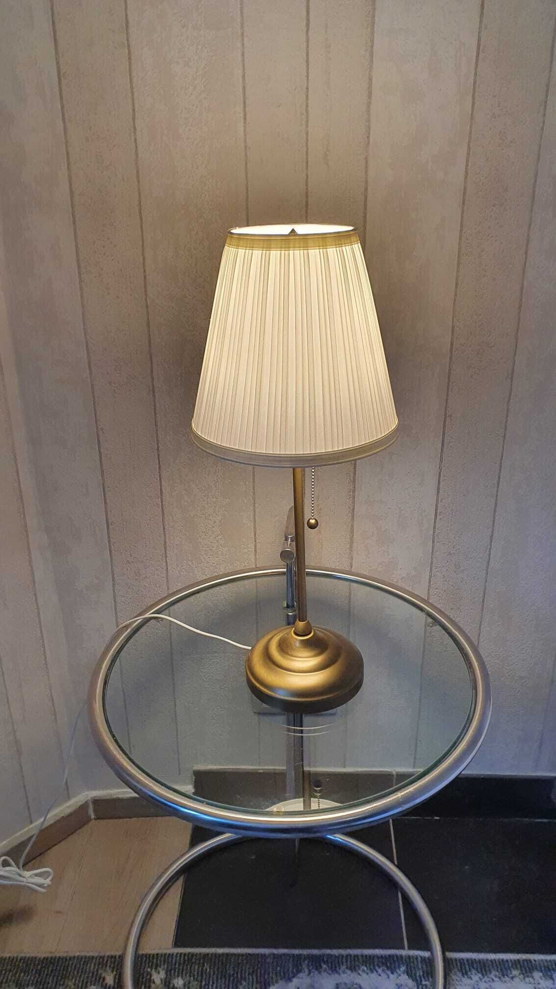 Een tafellamp met een plooilampenkap op een glazen tafel.