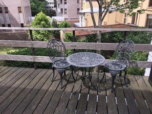 Eine Holzterrasse mit einem Metalltisch und -stühlen, mit Blick auf einen Garten und Gebäude.