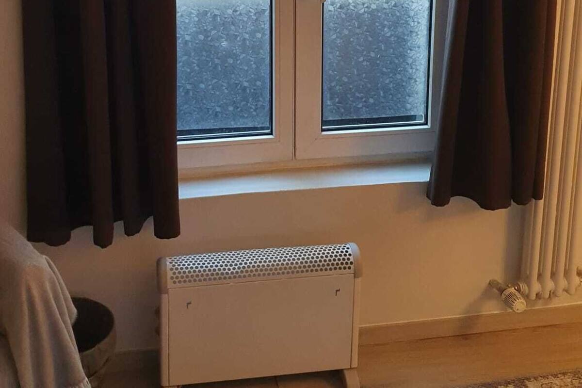 Una habitación con ventana, radiador y alfombra.