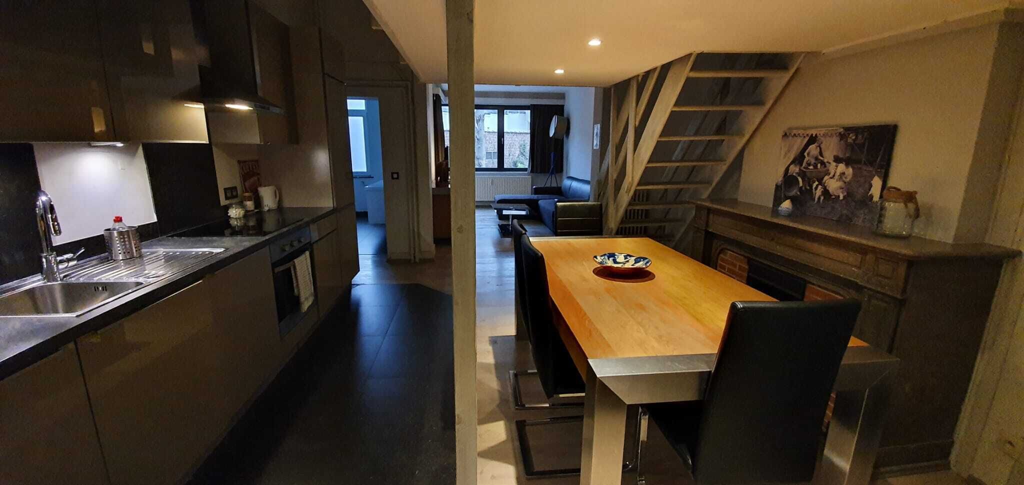 A modern kitchen with a central island, a dining area with a wooden table, and a staircase leading to an upper level.