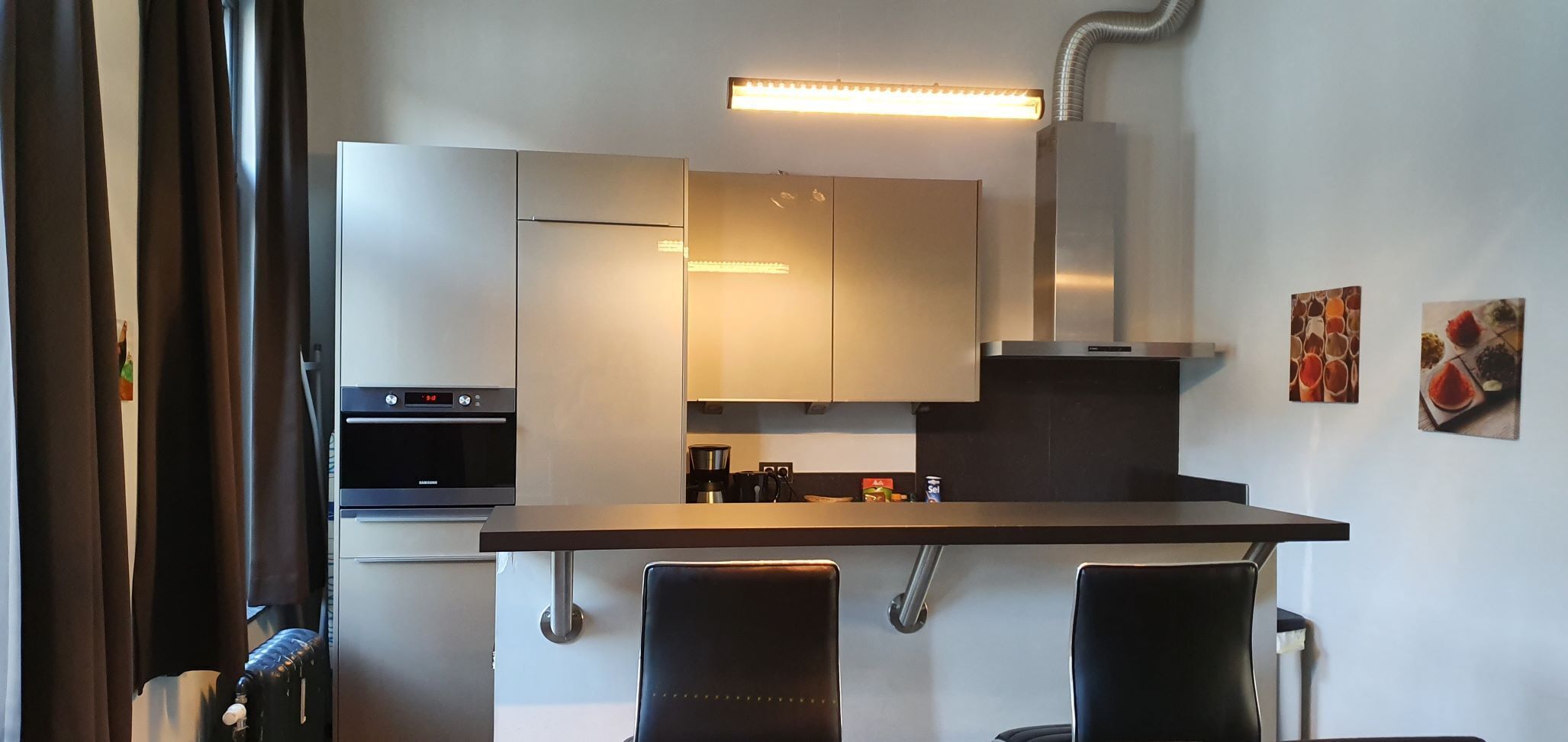 Une cuisine moderne dotée d’appareils électroménagers en acier inoxydable, d’un îlot central et de deux chaises noires.