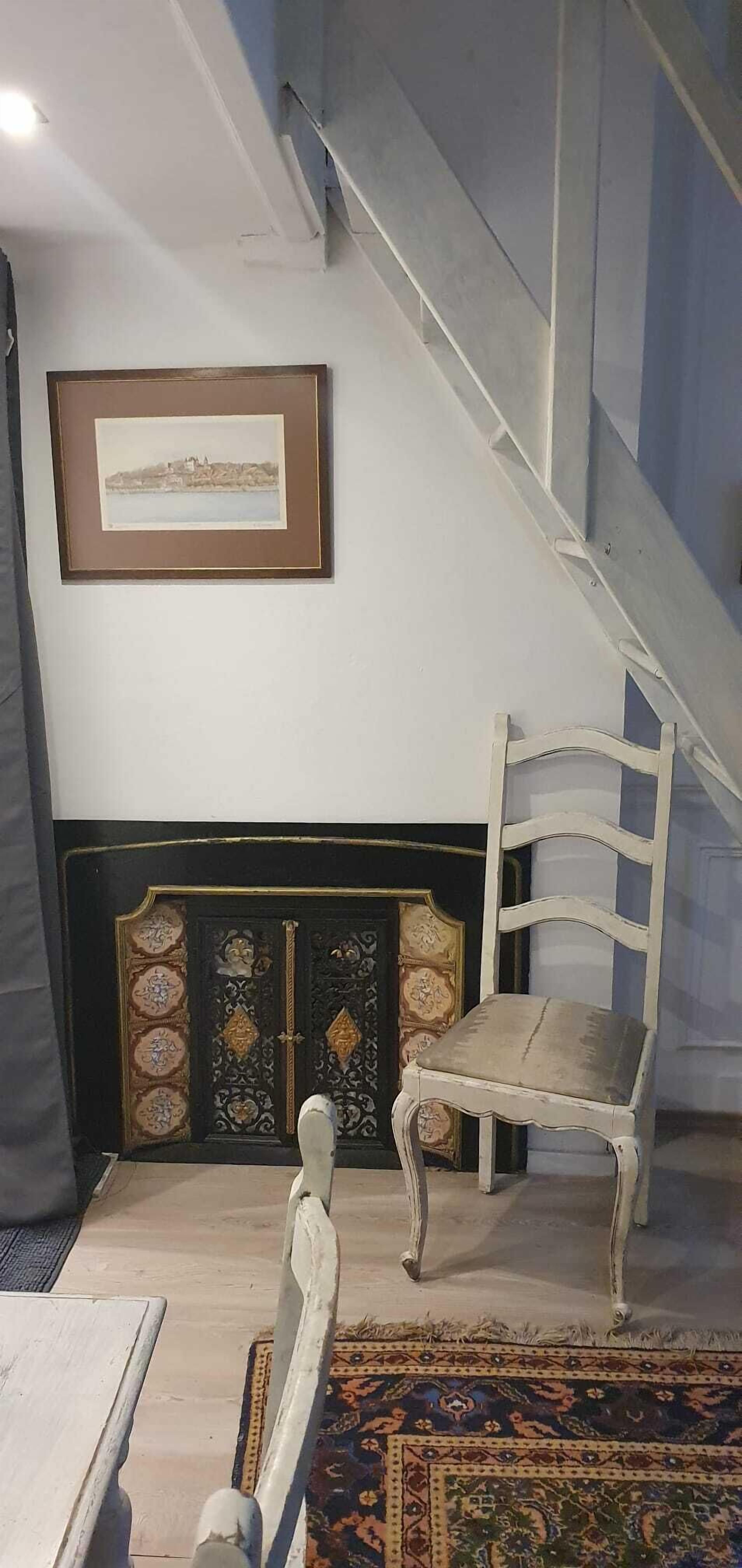 A room with a staircase, a framed picture on the wall, a patterned rug, and a decorative cabinet.