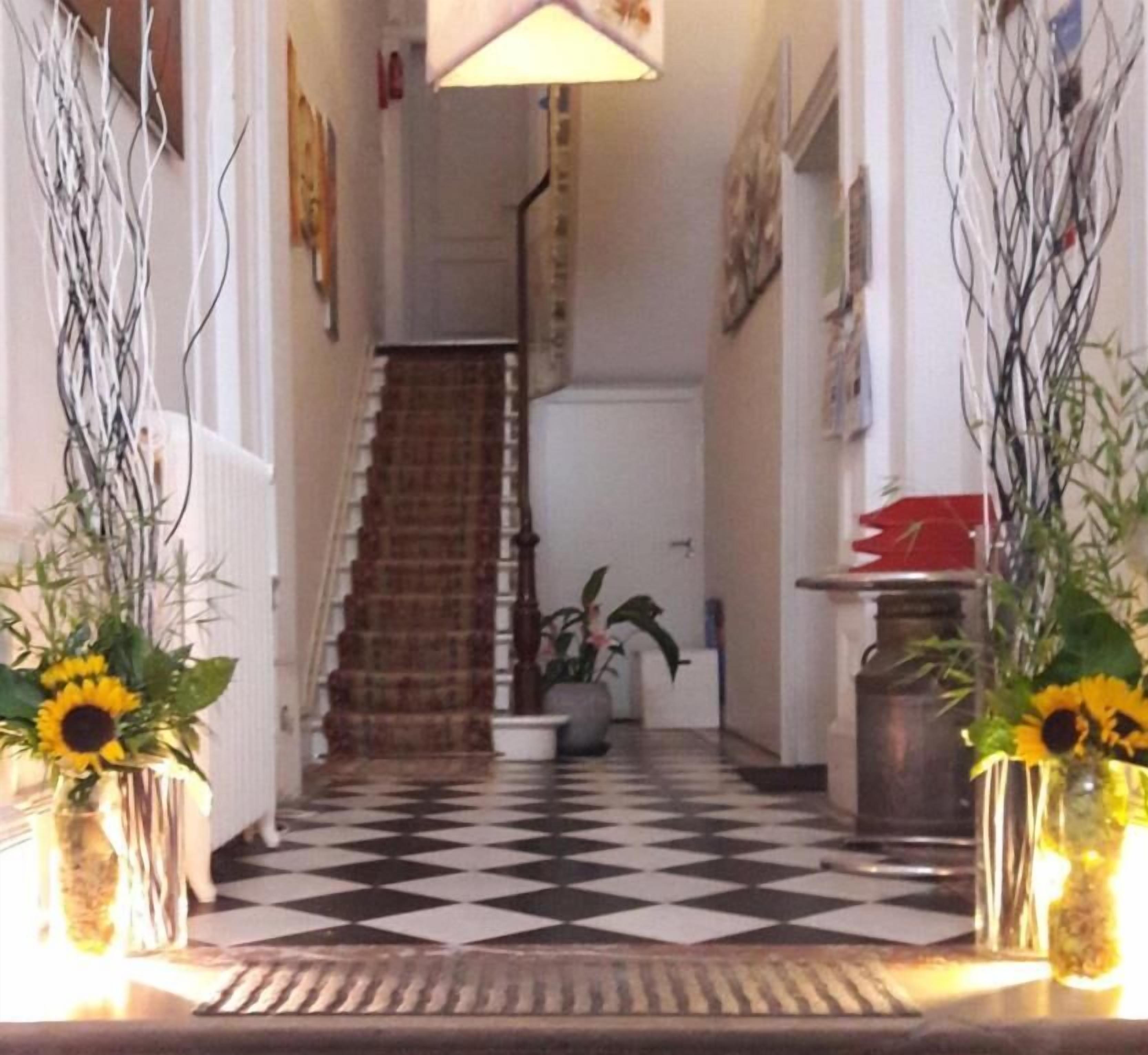 A hallway with a checkered floor, a staircase, and two vases with sunflowers.