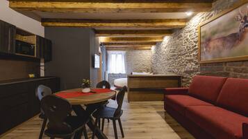 A cozy dining area with a wooden table and chairs, a red sofa, and a stone wall with a deer painting.
