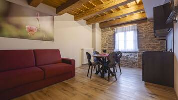 Una habitación acogedora con sofá rojo, mesa de comedor de madera, sillas y pared de piedra.