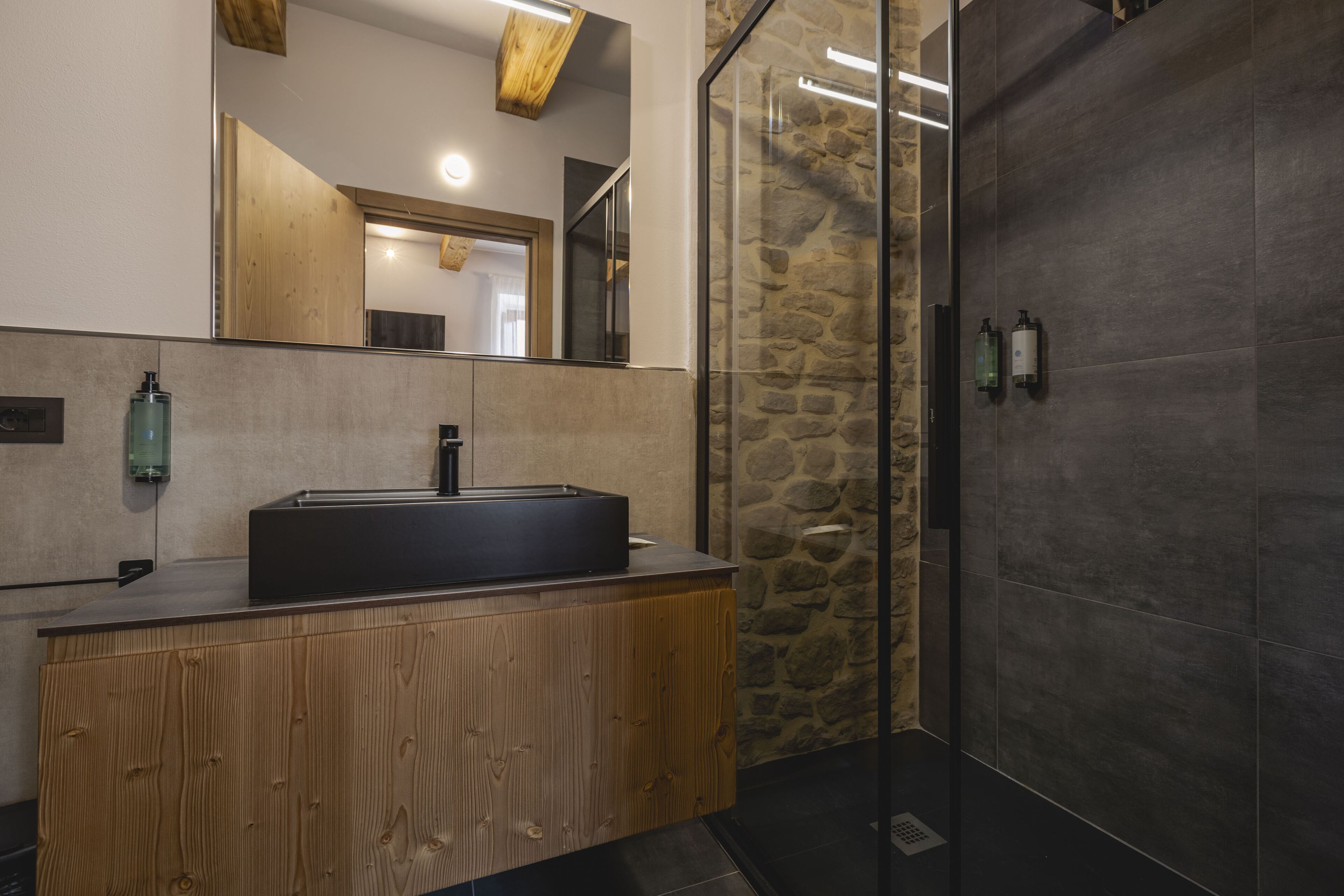 A modern bathroom with a wooden vanity, a large mirror, and a stone wall.
