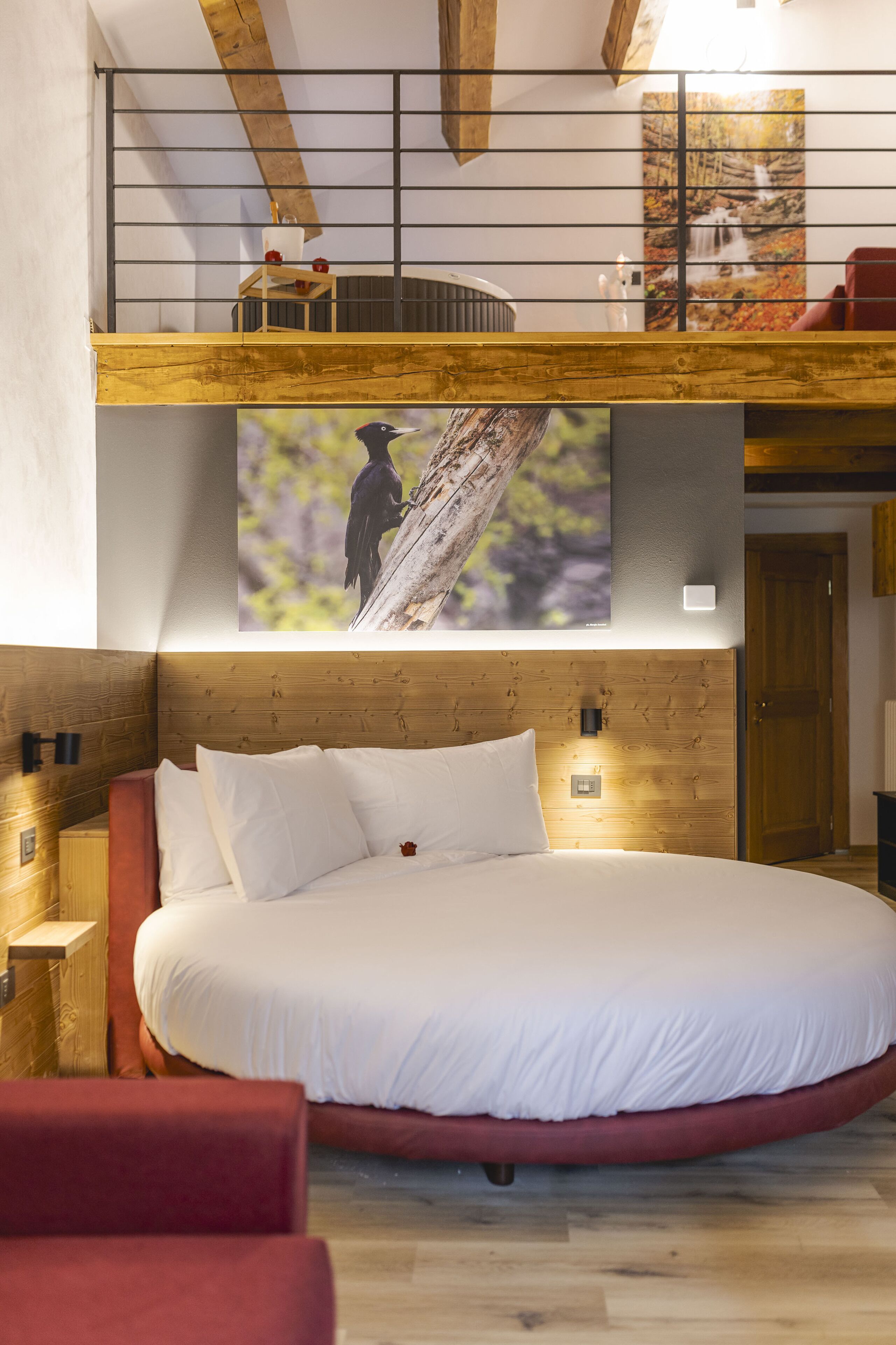 A bedroom with a large bed, wooden headboard, and a loft area with a view of a waterfall.