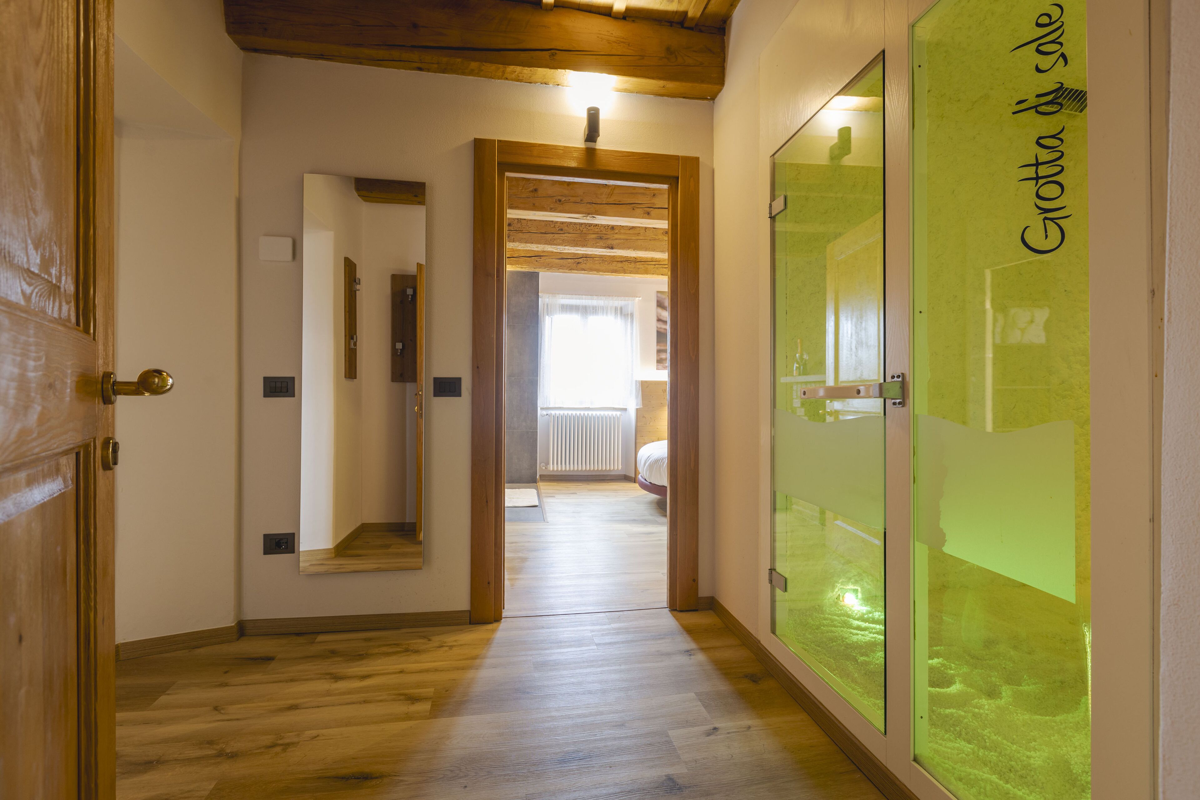 Un pasillo con suelo de madera y una puerta de vidrio verde con el texto 'Crotta di Sole'.